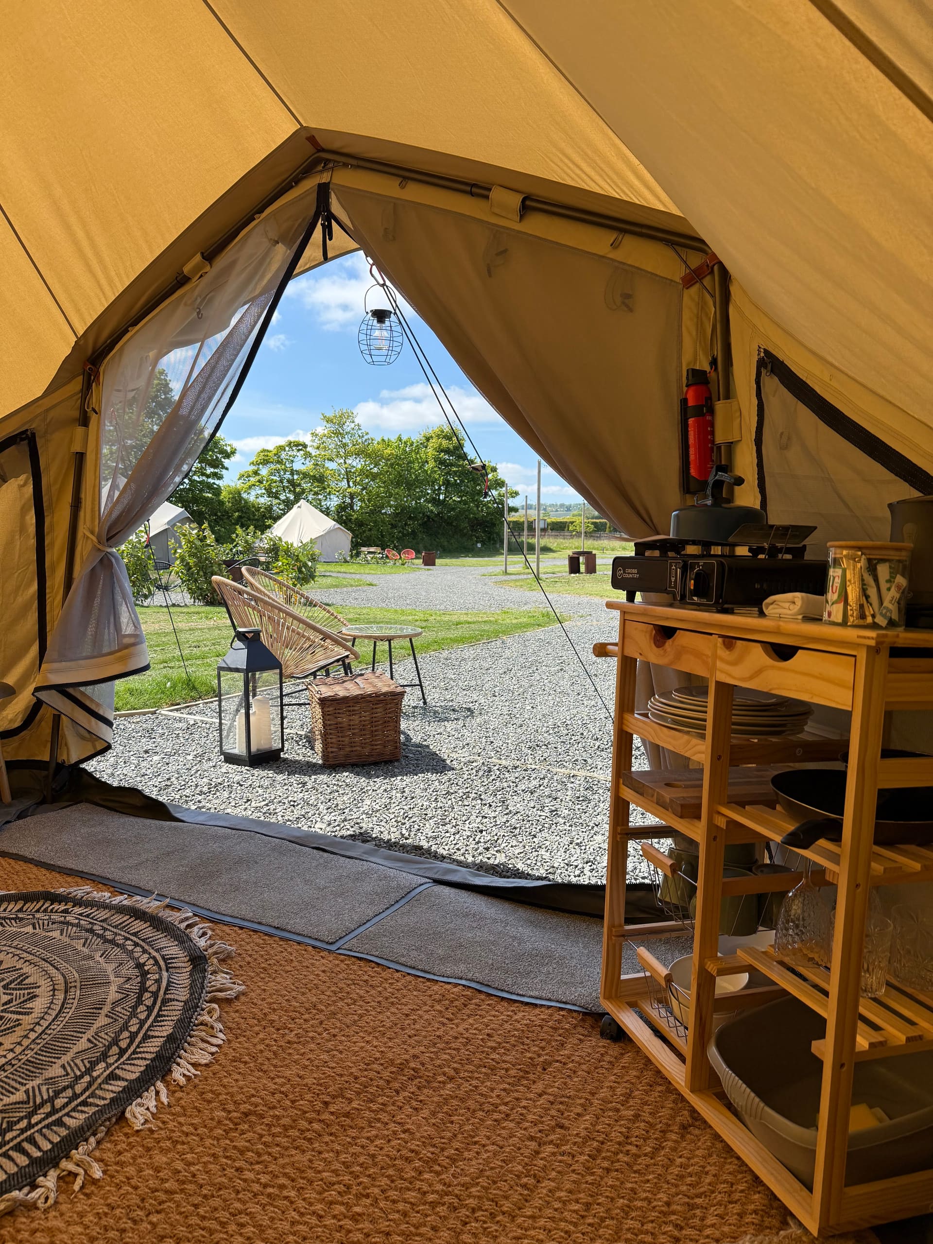 Inside a glamping bell tent at Coast and Castles — rugs, kitchenette and view of the site