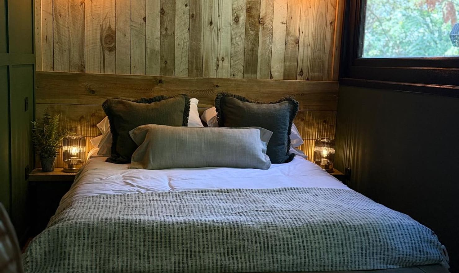 Luxury double bed inside The Bolt Hole at Coast and Castles with wooden panelled headboard, wall sconces and warm lighting