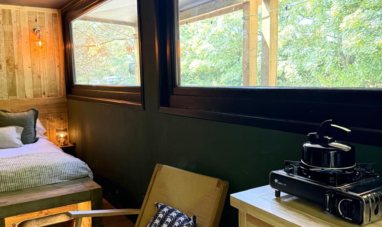 Inside The Bolt Hole at Coast and Castles showing the kitchenette, rattan chair and panoramic woodland windows