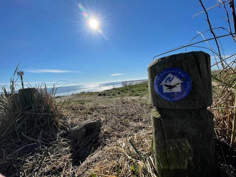 St Oswald's Way coastal path sign with the Northumberland coast and sea behind it
