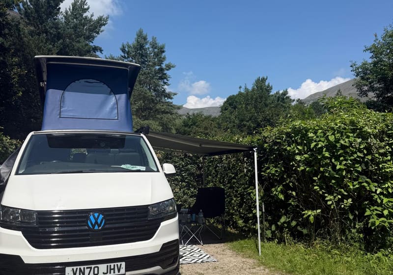 Cuddy with pop-top raised and side awning extended at a campsite