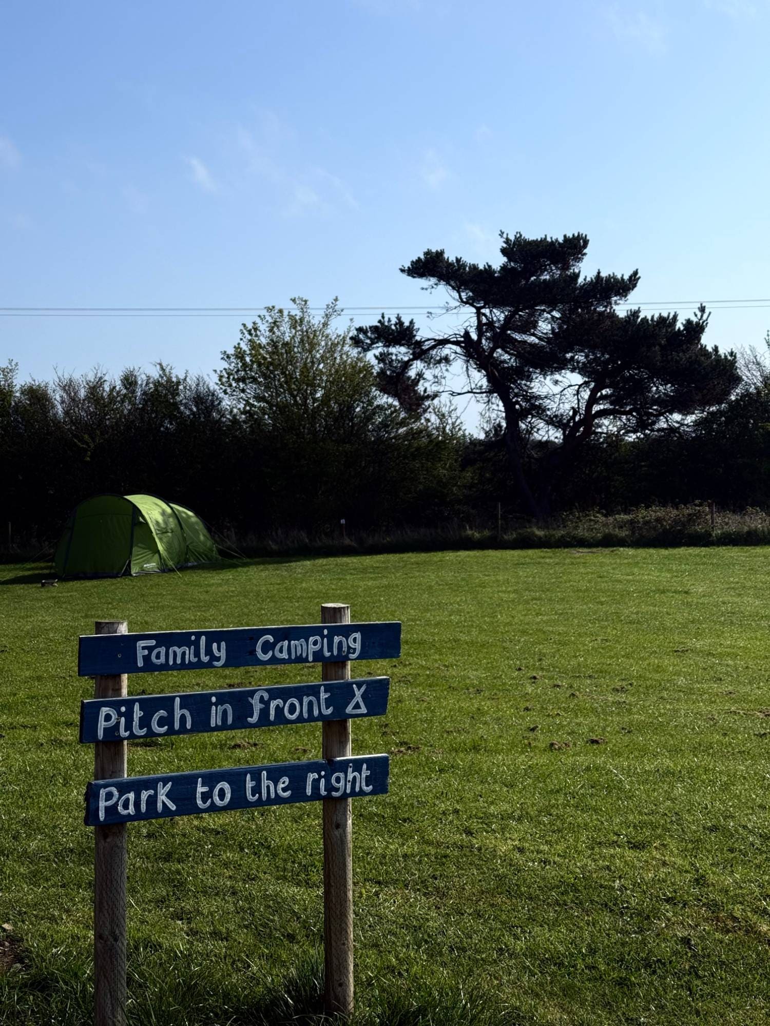 A family camping pitch sign next to a green tent on the grass field at Coast and Castles