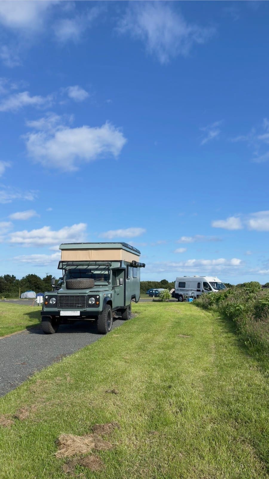 A Land Rover campervan parked on a grass pitch at Coast and Castles with campervans in the background