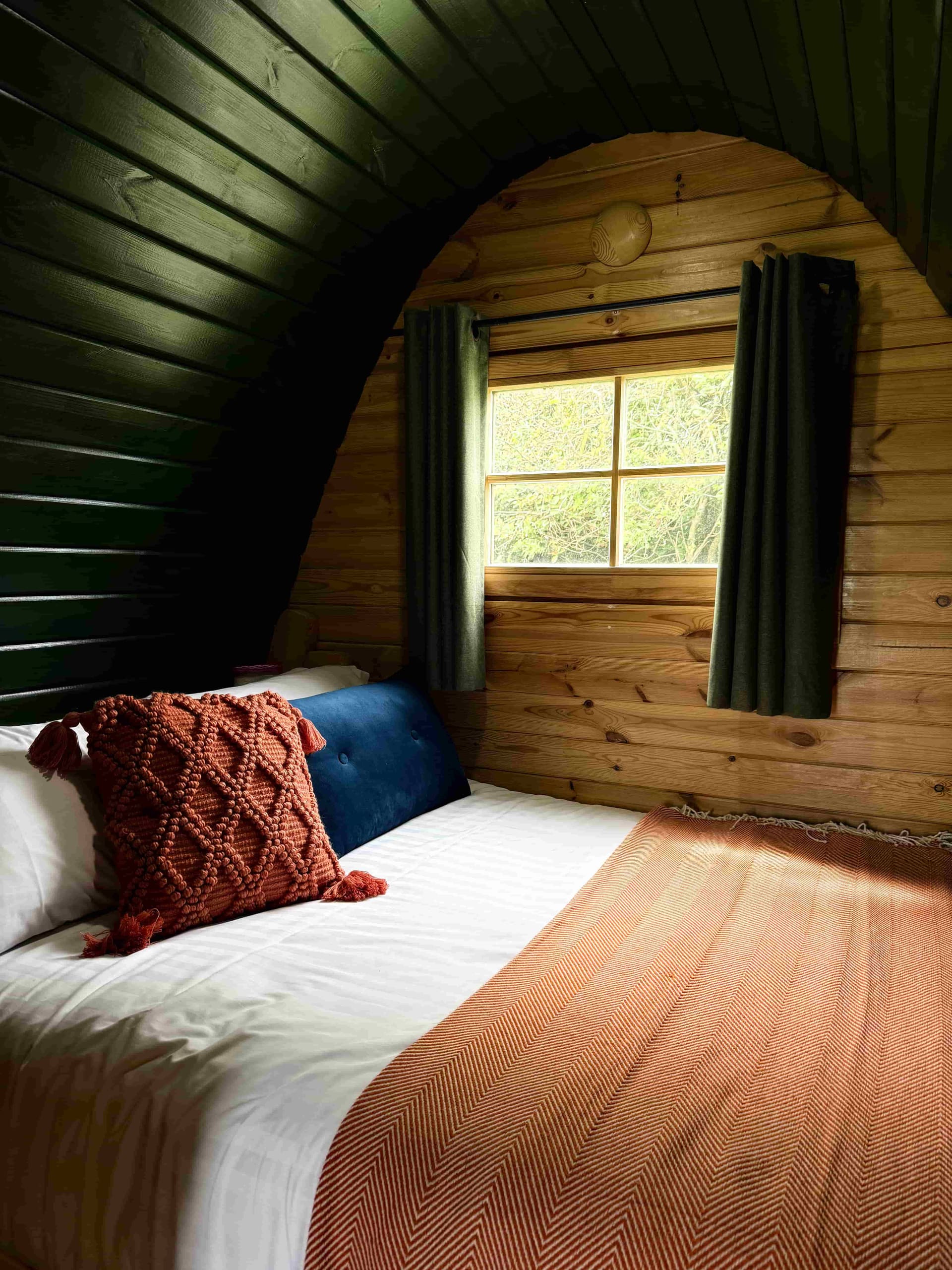 Double bed inside a glamping pod at Coast and Castles with warm lighting and arched wooden ceiling