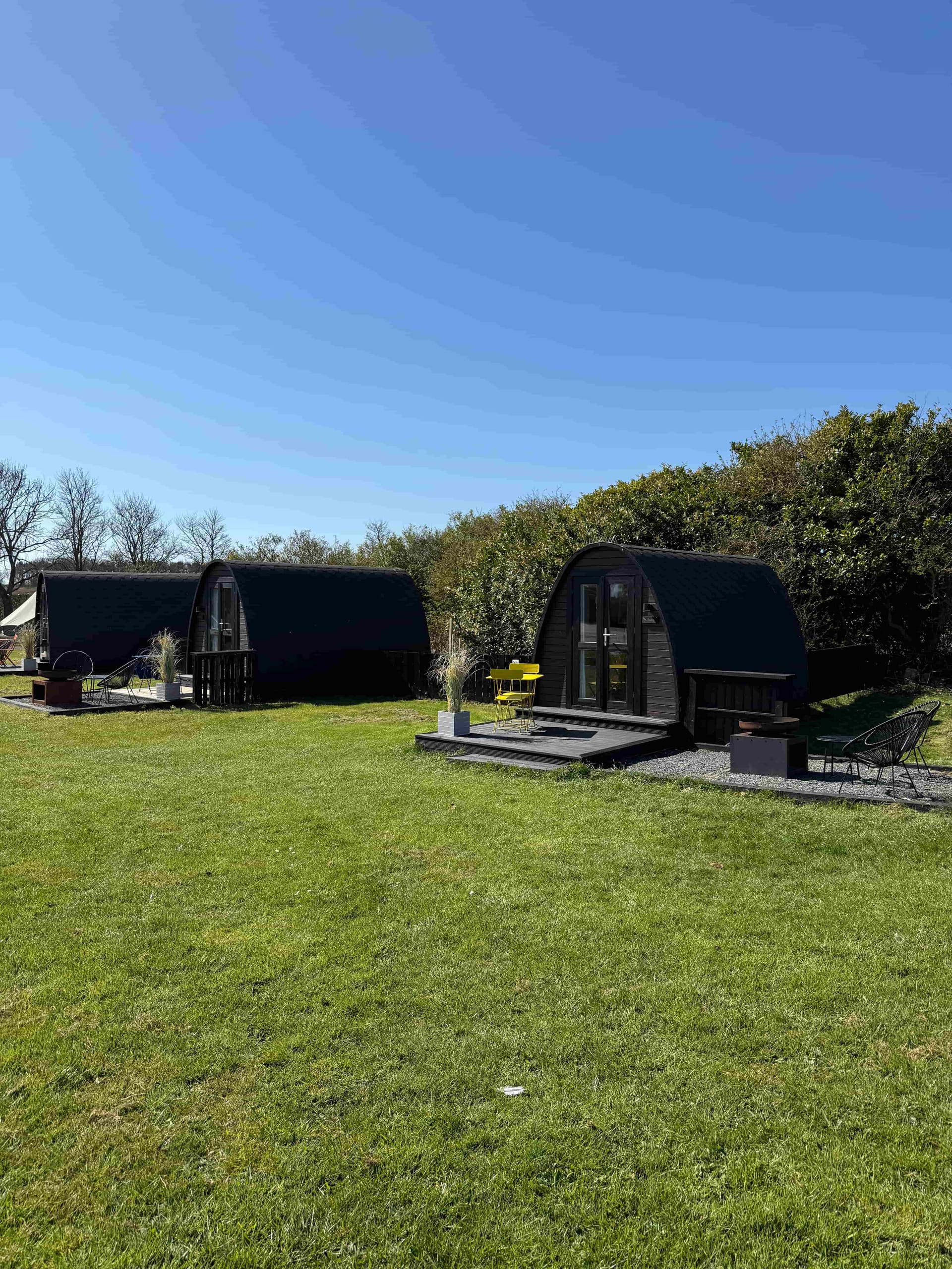 Two timber glamping pods at Coast and Castles with private decking and outdoor seating on a sunny day